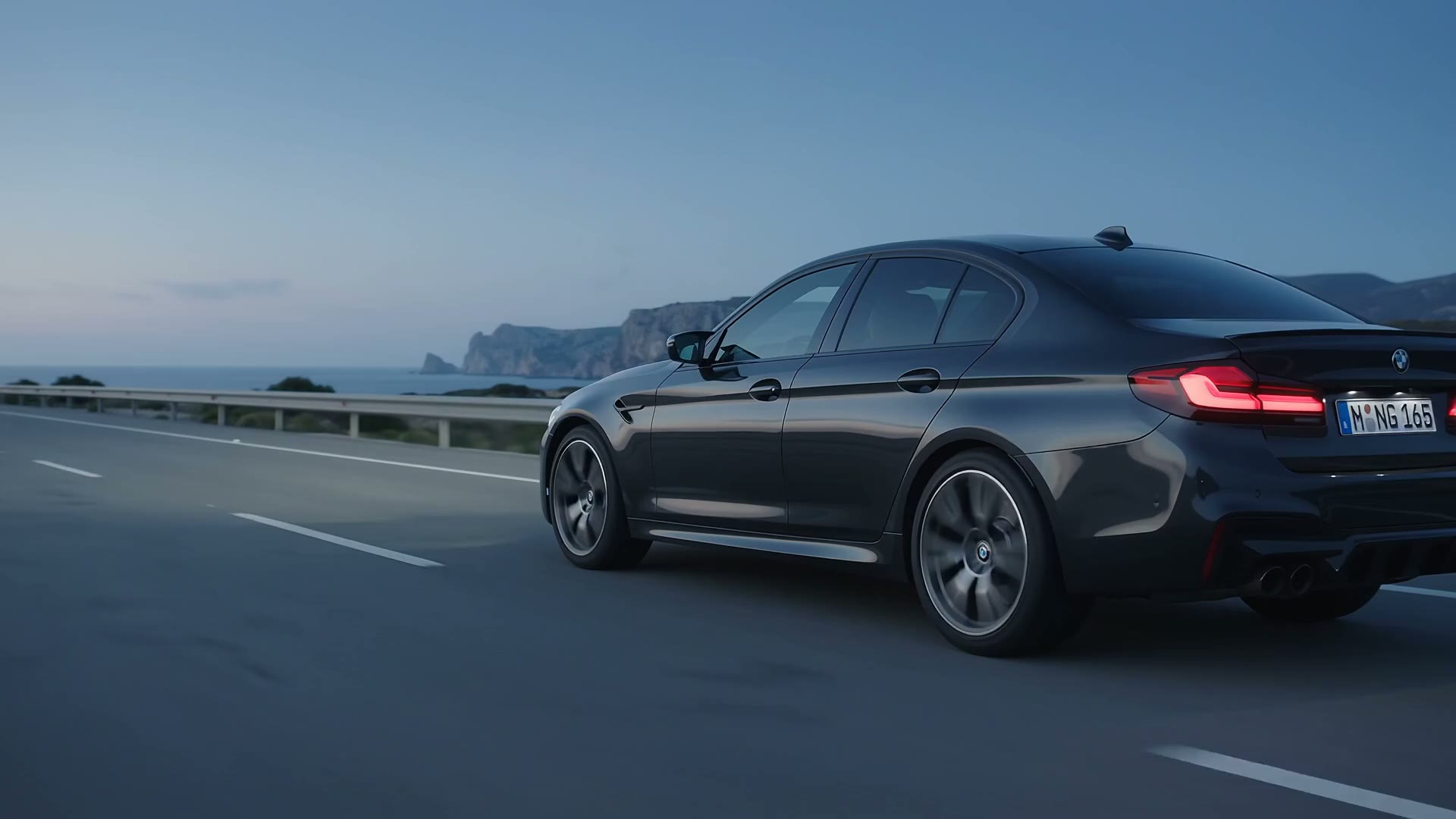 Berlina alemana gris oscuro circulando por una carretera costera al atardecer